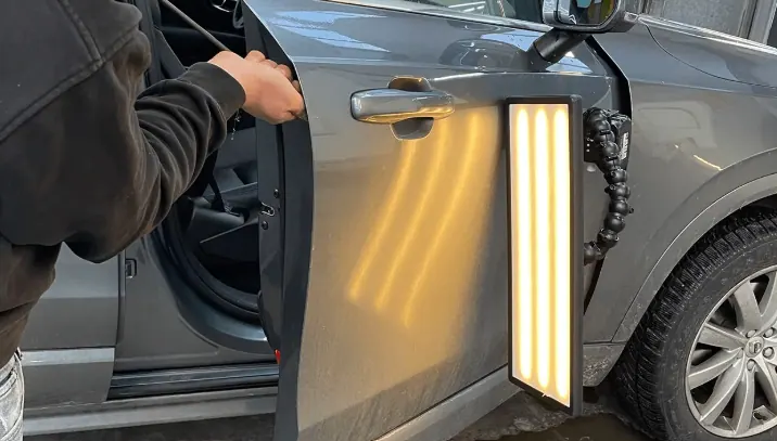 Lack Attacke Service - Techniker entfernt Delle mit Spezialwerkzeug und Lichtreflektor von Autotür